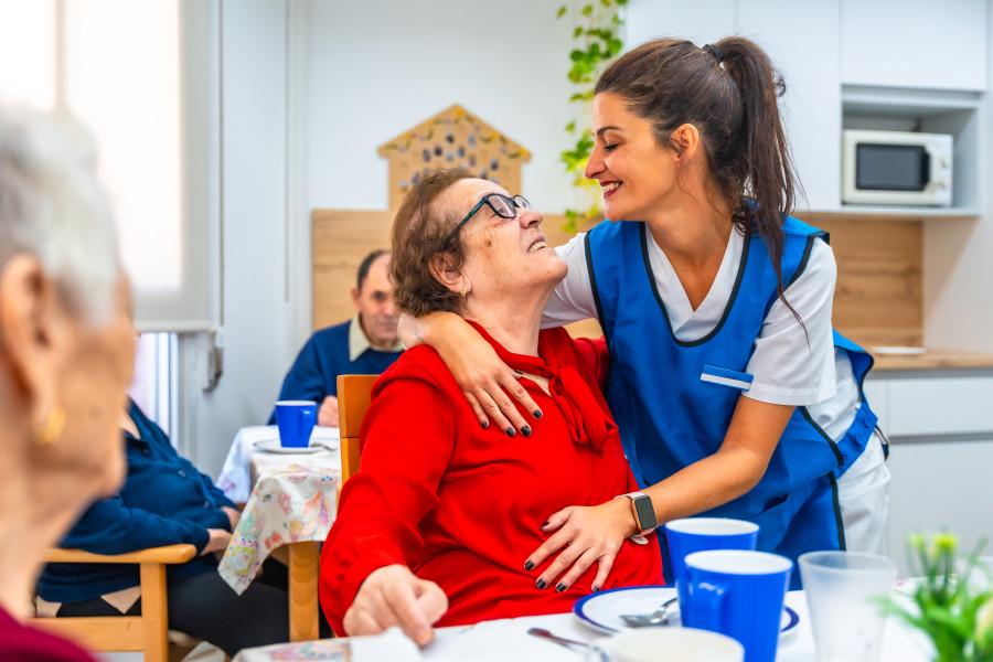 A carer and an aged care resident sharing a warm hug at the dining table