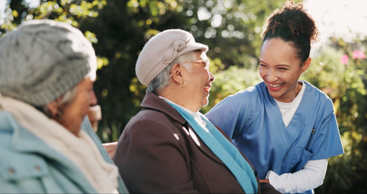 A smiling nurse shares a laugh with an elderly woman outdoors