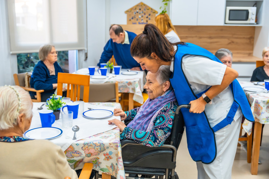 A carer chatting warmly with an aged care resident in a wheelchair at a dining table
