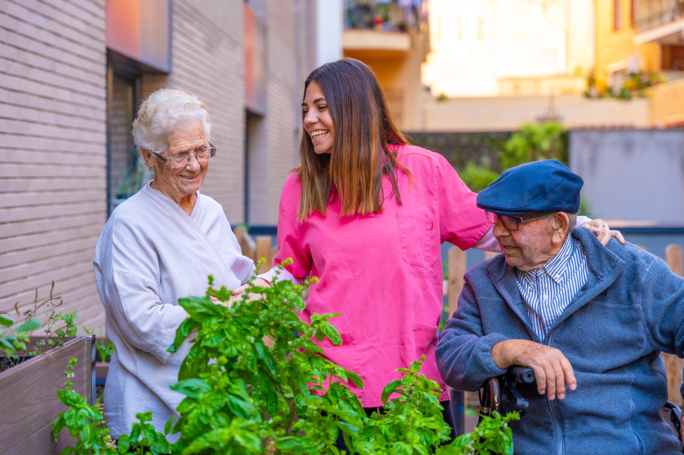 Trained student volunteer chatting with elderly aged care residents in a sunny garden during a Generations Connect visit