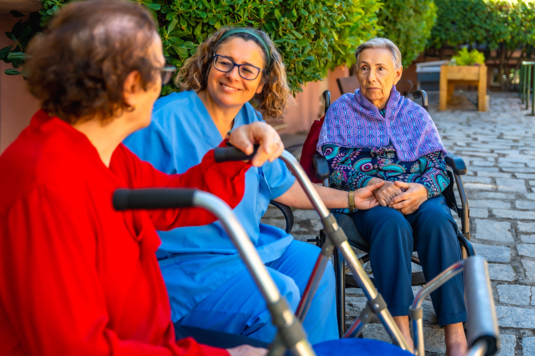 A student volunteer sitting outdoors in conversation with two aged care residents