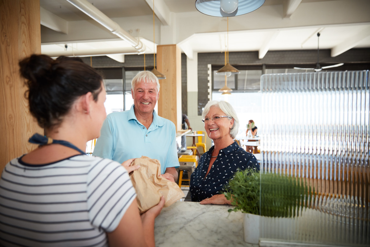 A senior couple smiling as they are served at a cafe counter